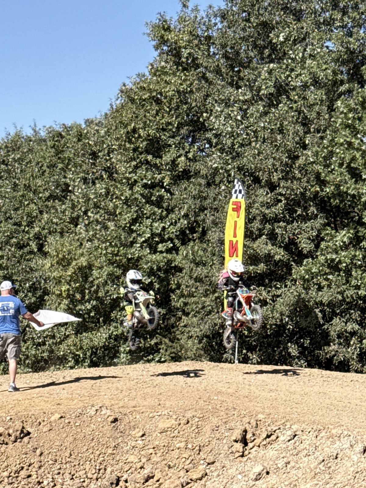 Two young riders in the air over a jump near the finish flag
