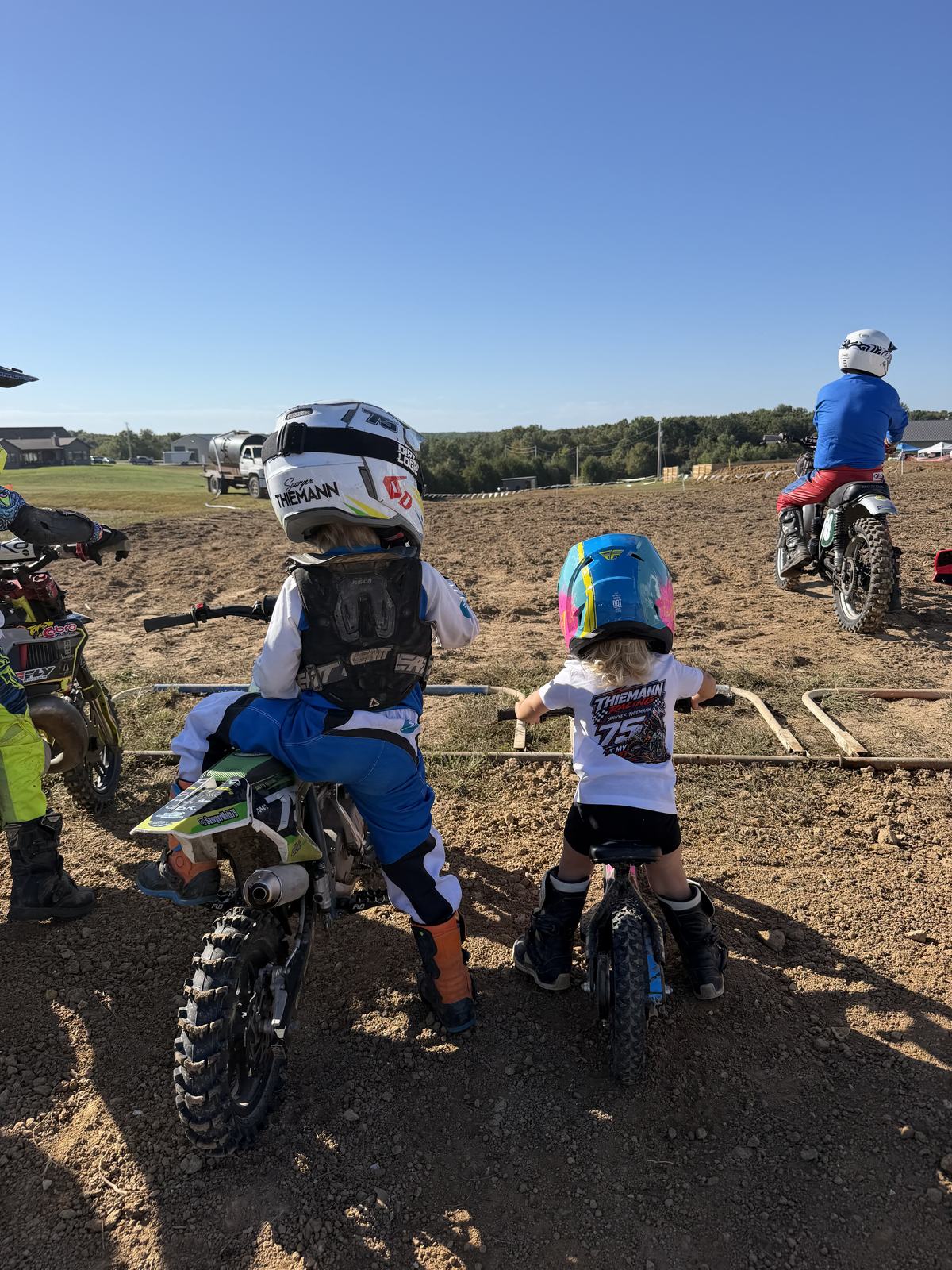 Sawyer in his #75 Thiemann jersey on his green bike next to his little sister on her balance bike at the starting gate